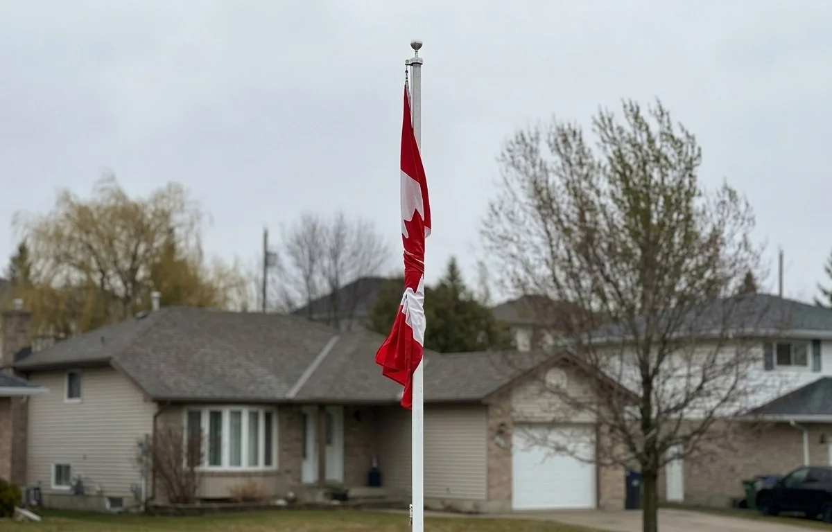 A Canadian flag flown on a classic rope-and-pulley flagpole. The flag has tangled and wrapped itself around the pole due to the wind.