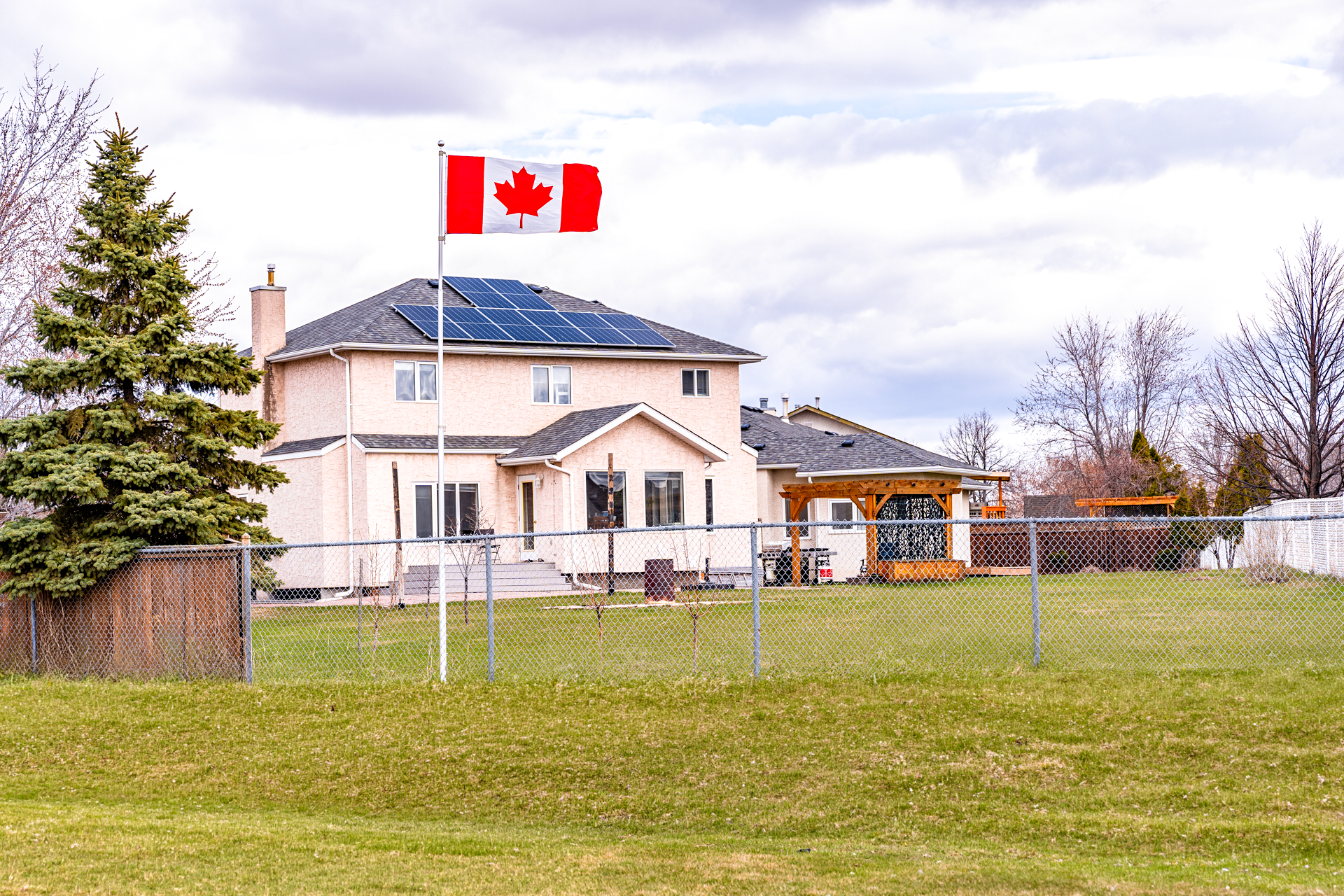 A Titan telescoping flag pole with a white anodized finish flying a Canadian flag in the backyard of a house in Winnipeg.