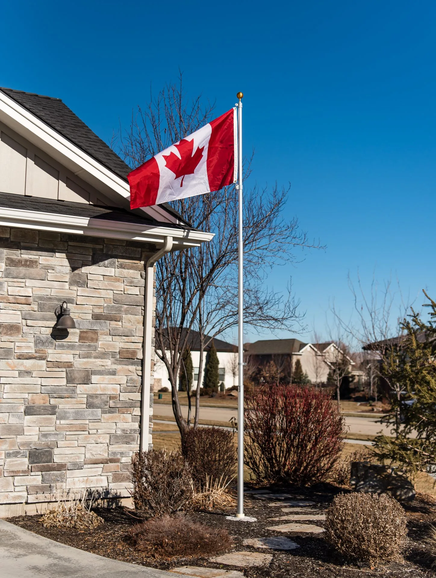 A 15 foot flagpole with a silver anodized finish provided by The Flag Shop. It is installed outside a house and is flying the Canadian flag.