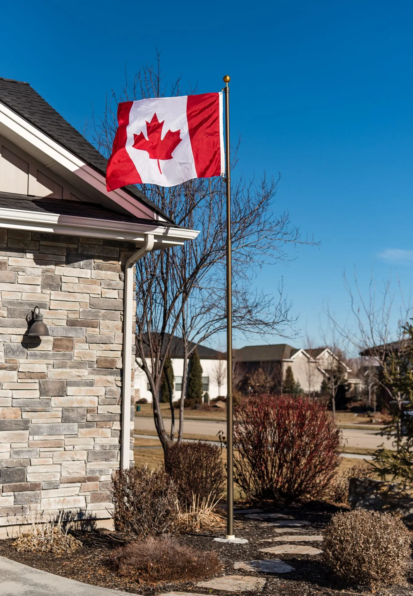A 15 foot Titan telescoping flagpole with a dark bronze finish provided by The Flag Shop. It is installed outside a house and is flying the Canadian flag.