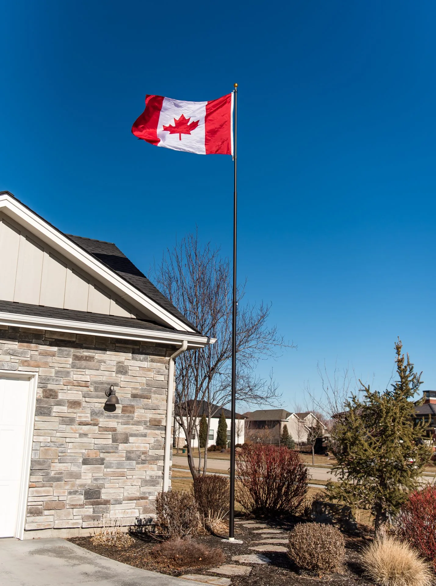 A 25 foot Titan telescoping flagpole with a dark bronze finish provided by The Flag Shop. It is installed outside a house and is flying the Canadian flag.