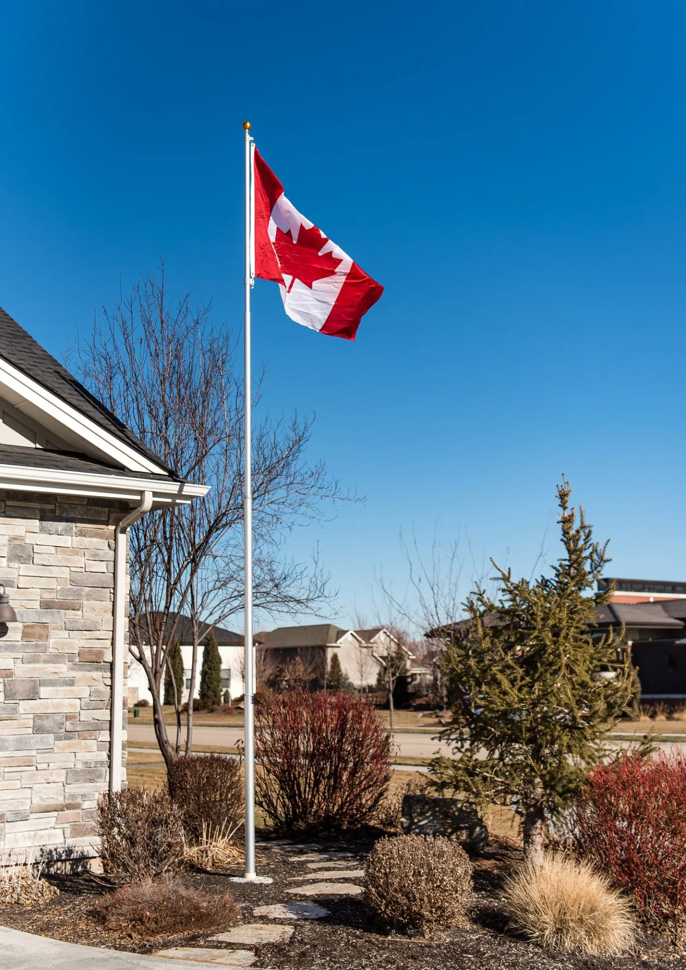 A 20 foot Titan telescoping flagpole with a silver anodized finish provided by The Flag Shop. It is installed outside a house and is flying the Canadian flag.